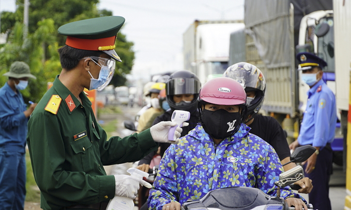 A police officer checks body temperatures of travelers at a Covid-19 checkpoint in Tien Giang Province, July 8, 2021.
